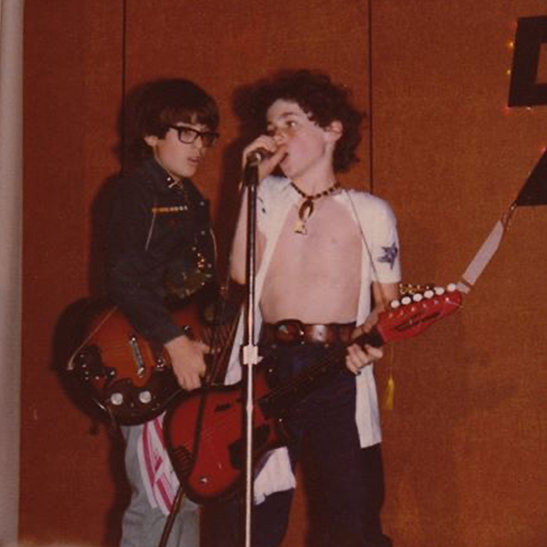 Young Rob Johnston singing into a microphone with a red electric guitar